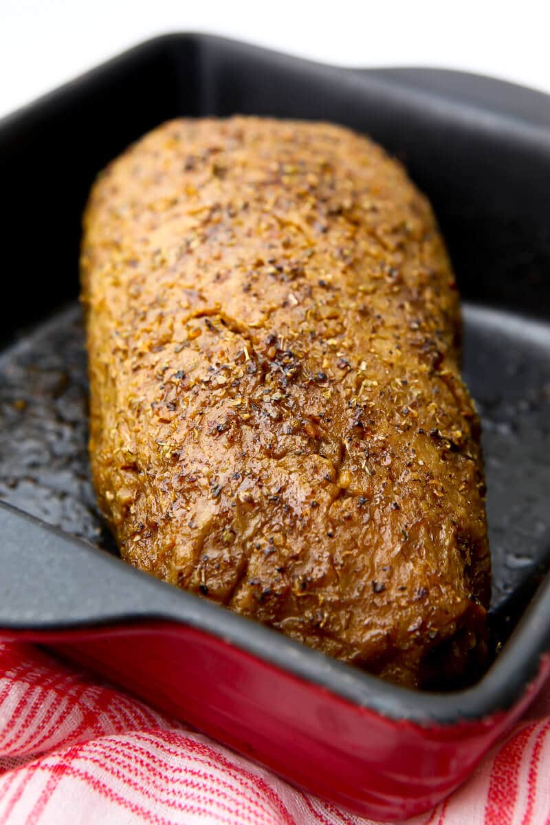 A roasted vegan turkey that has been based with spices in a red baking pan.