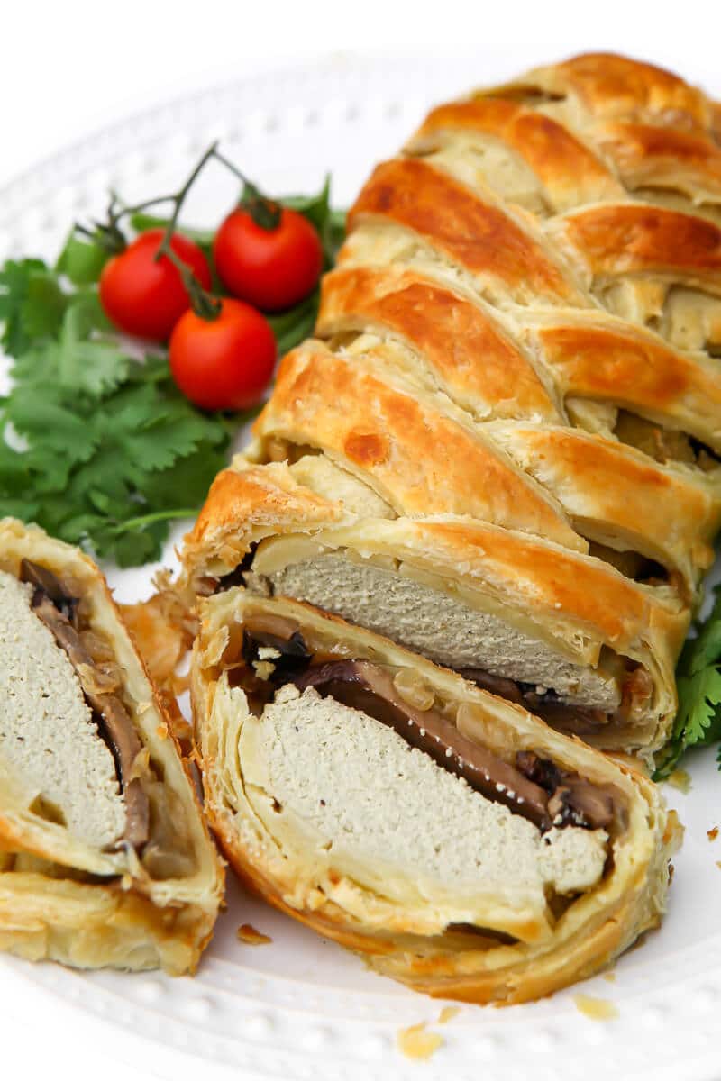 A top view of a vegan wellington with a braded top with 2 slices cut off of it.