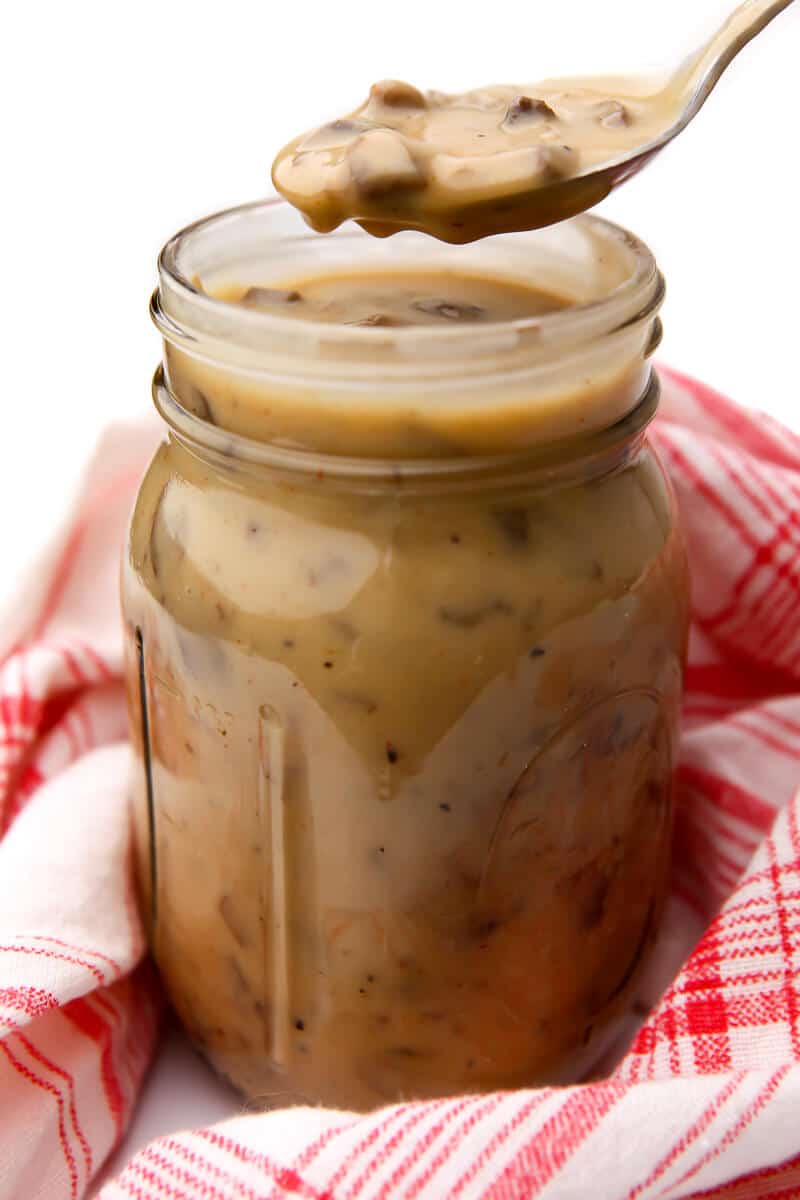 A jar full of condensed vegan cream of mushroom soup with a spoonful being taken out of it.