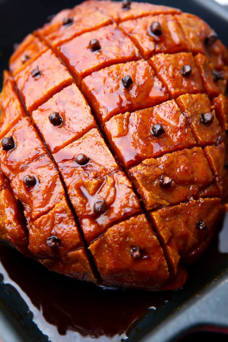 A seitan ham in a roasting dish with cloves in it and a sweet glaze on top.