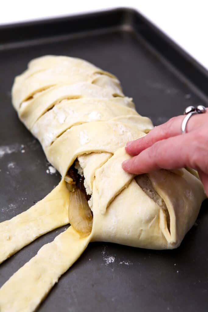 Braiding the strips of puff pastry on top of the vegan wellington.