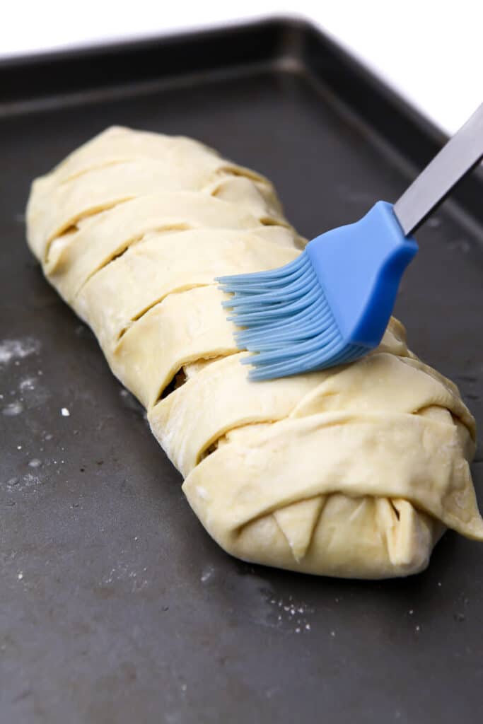 Brushing the top of the vegan wellington with aquafaba before baking.