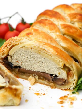 A vegan wellington filled with onions, mushrooms, and tofu on a white plate with a slice cut out of it.