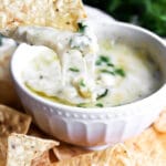 A white bowl filled with easy vegan artichoke dip topped with vegan cheese and parsley.