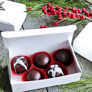 A box of homemade vegan chocolates with pine boughs and berries around it.