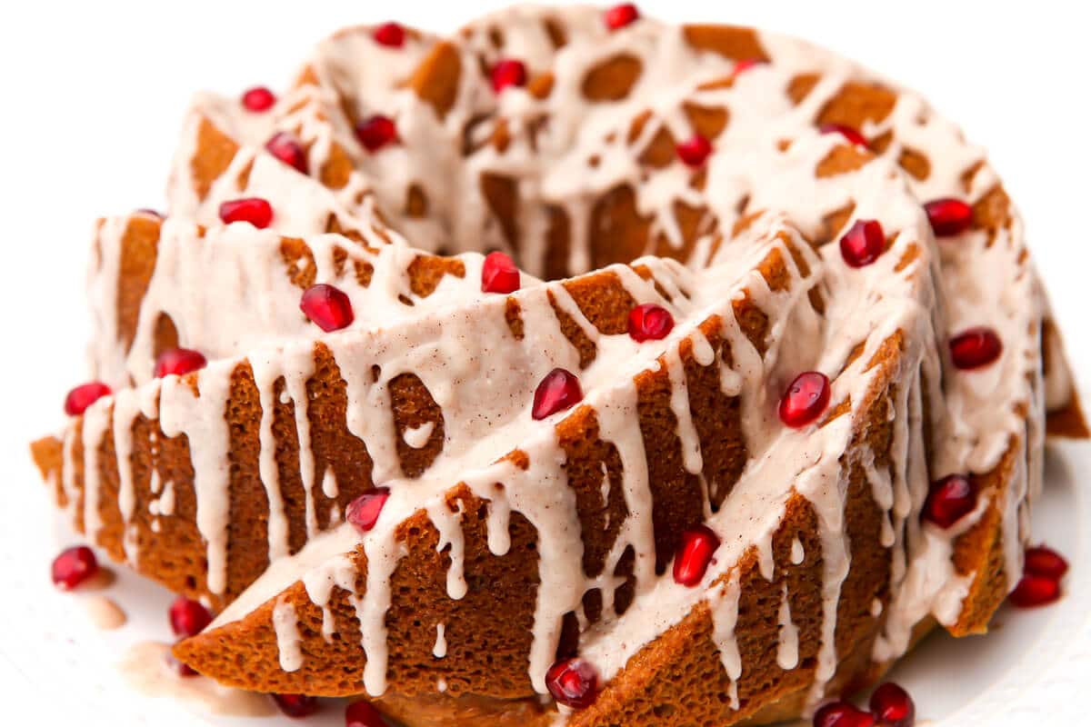 A vegan bundt cake with icing and pomegranates on it.