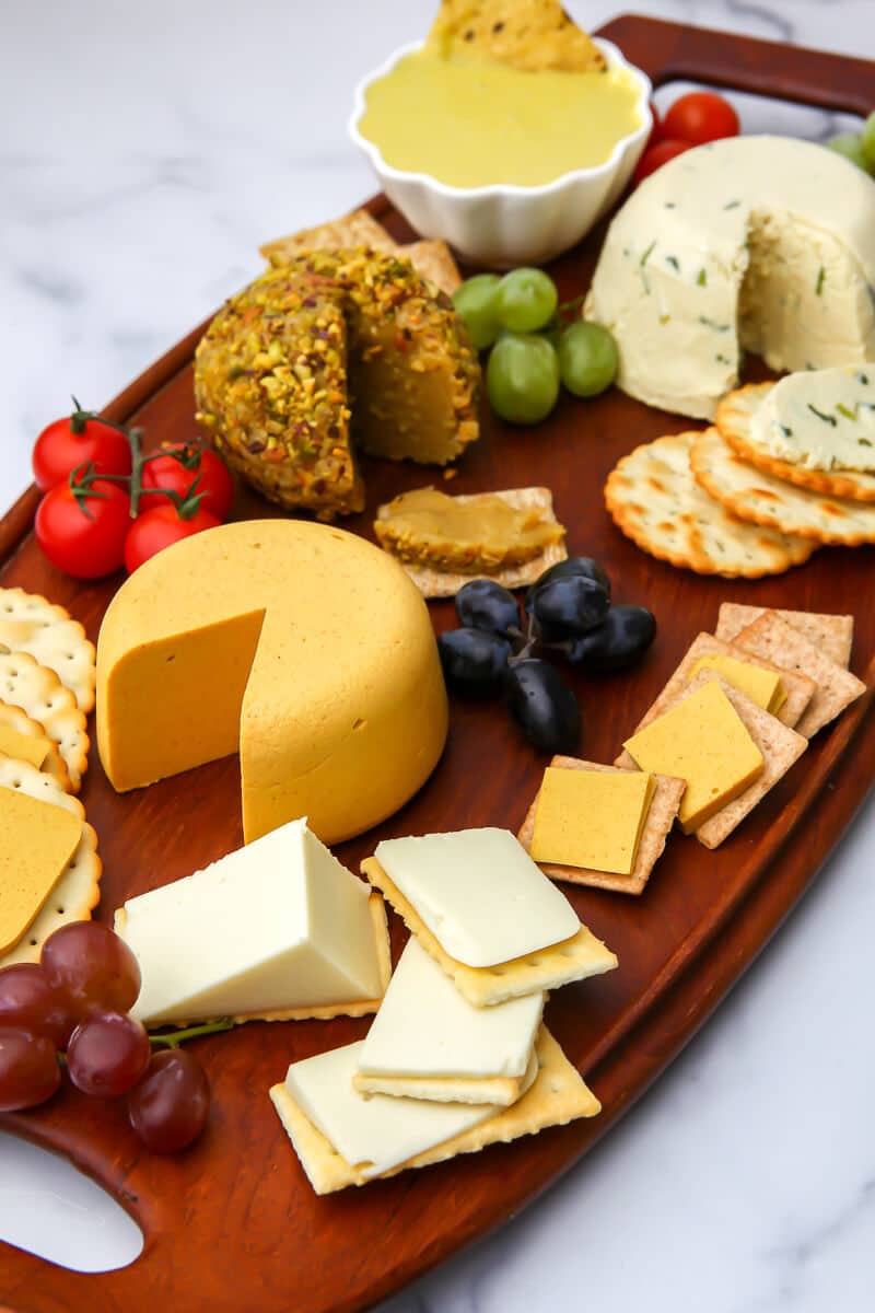 A wooden board filled with vegan cheeses, crackers, and grapes.