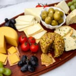 A vegan cheese board filled with a variety of vegan cheeses, cherry tomatoes, olives, and grapes.