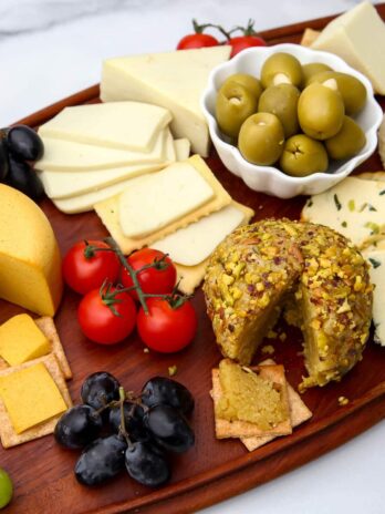 A vegan cheese board filled with a variety of vegan cheeses, cherry tomatoes, olives, and grapes.