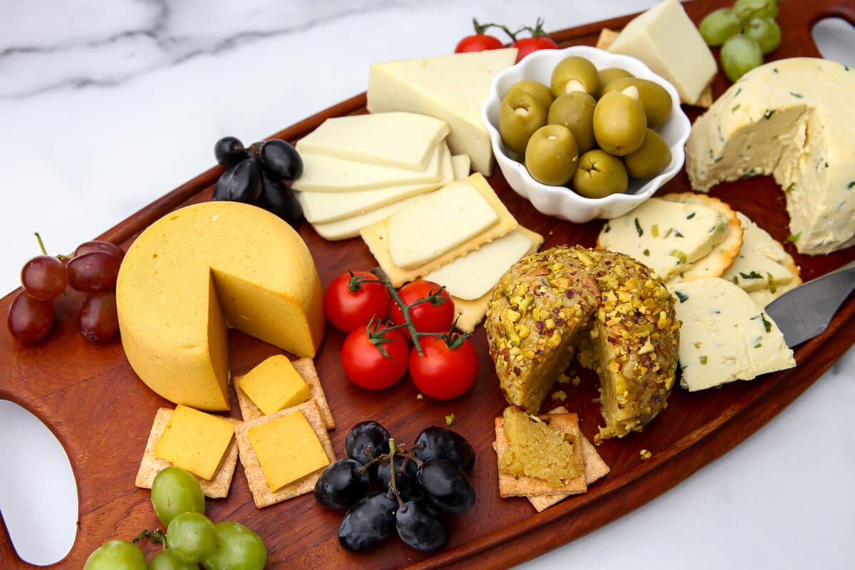 A wooden board filled with vegan cheeses, grapes, and olives.