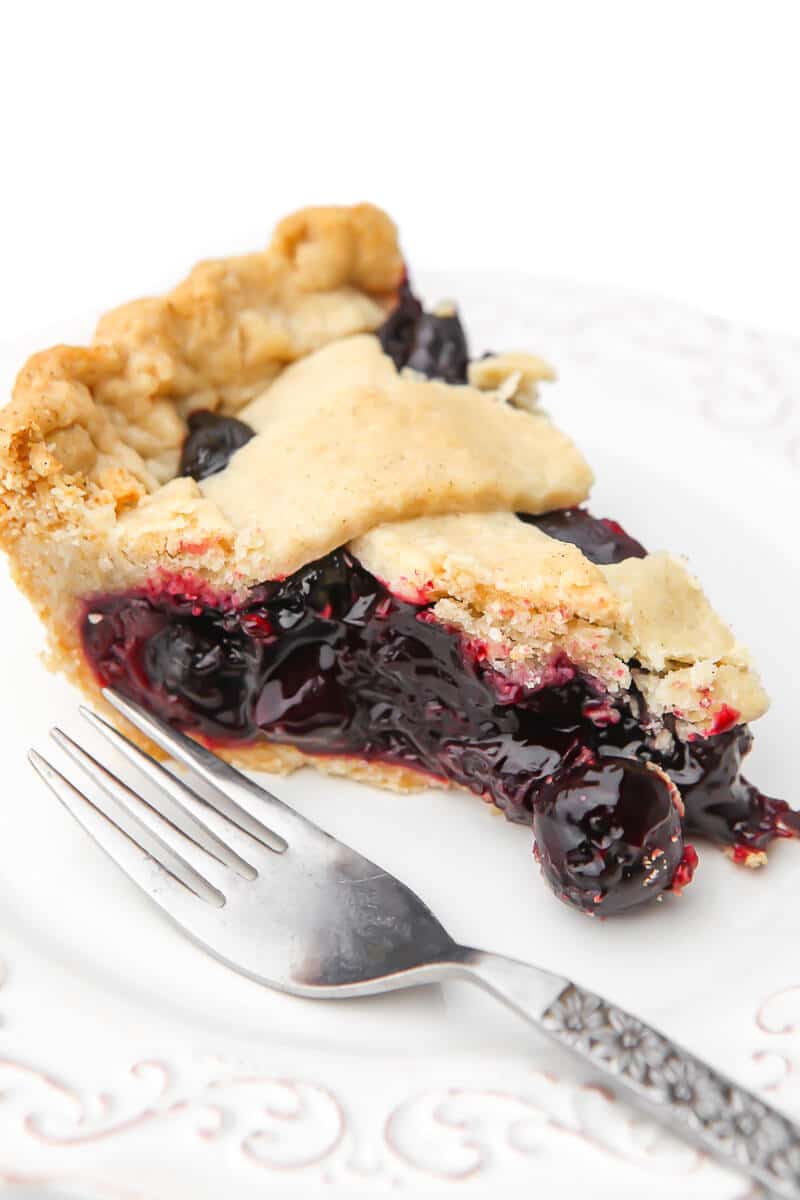 A slice of a cherry pie on a white plate with a fork on the side.