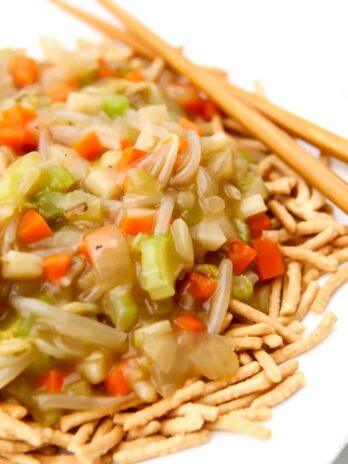 A close up of a white plate with chow mein noodles covered in vegetable chop suey.