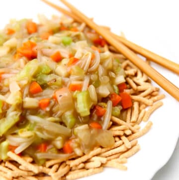 A close up of a white plate with chow mein noodles covered in vegetable chop suey.