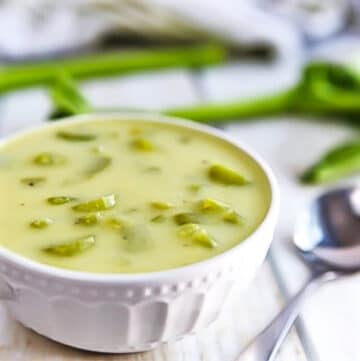 A close up of a bowl of vegan cream of celery soup with a spoon in it.