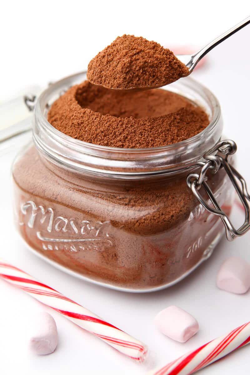A large mason jar filled with vegan hot chocolate mix with a spoon scooping some off the top.