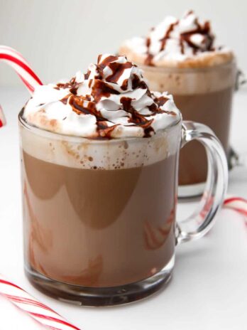 Two glass mugs full of vegan hot chocolate with whipped cream on top.