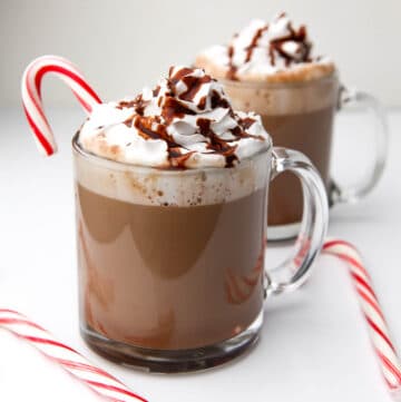 Two glass mugs full of vegan hot chocolate with whipped cream on top.