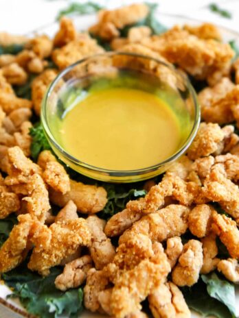 Vegan fried chicken strips on a bed of kale with vegan honey mustard dipping sauce.