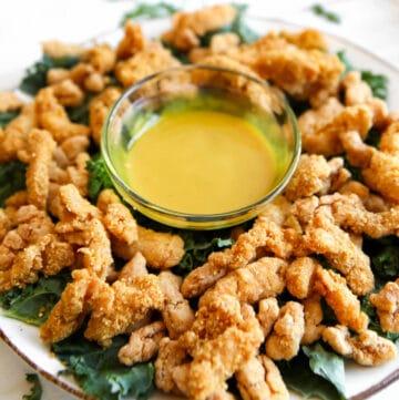 Vegan fried chicken strips on a bed of kale with vegan honey mustard dipping sauce.