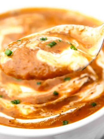 A white bowl filled with pumpkin bean soup with a spoonful above it.