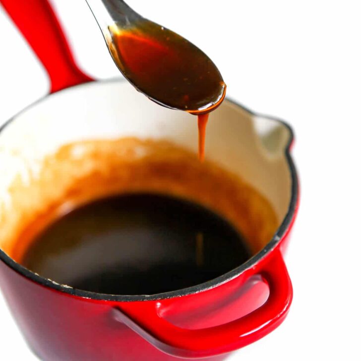 A red saucepan filled with homemade teriyaki sauce with a spoonful of it over top of it.