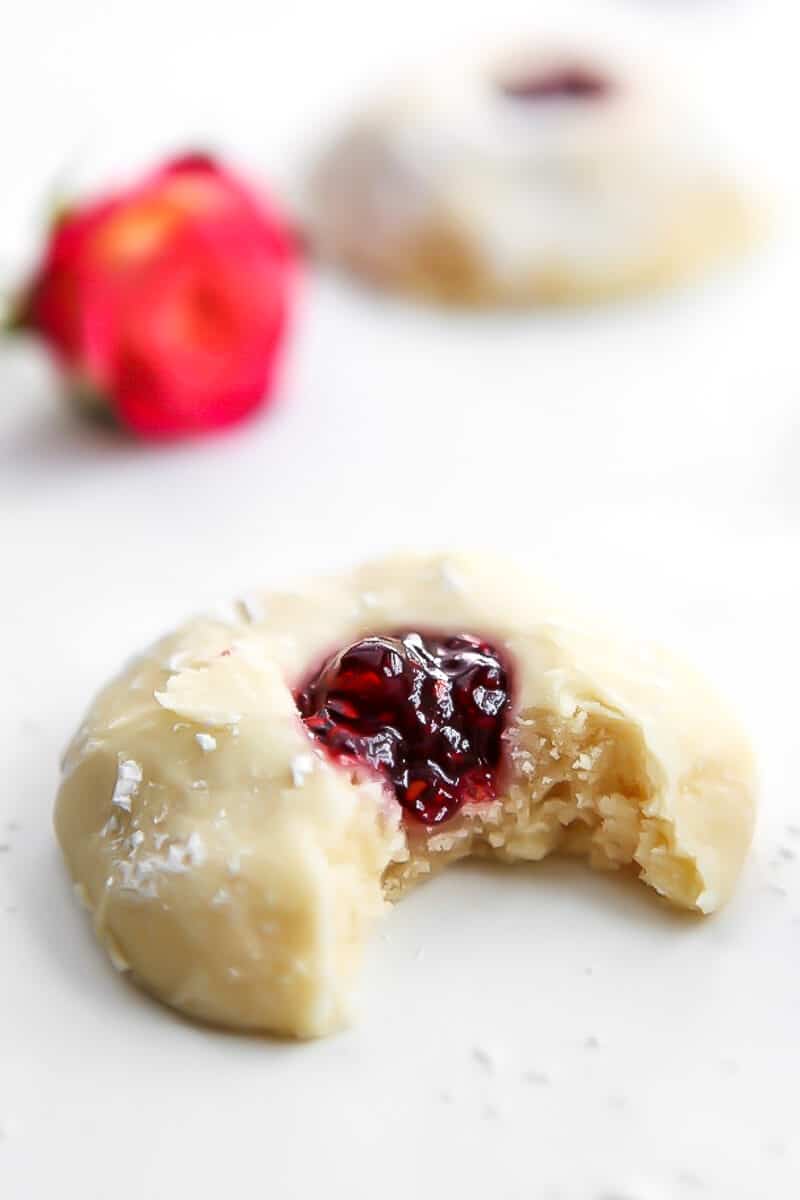 A gluten free vegan thumbprint cookie with jam in the middle with a bite taken out of it.