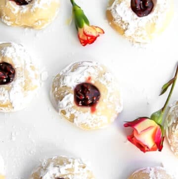 Vegan thumbprint cookies with raspberry jam in the middle on a white counter top.