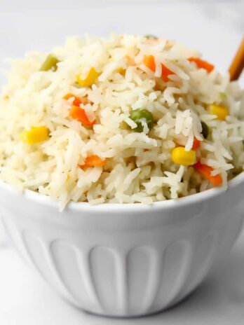 A white bowl filled with Thai coconut rice with carrots, corn, and peas.