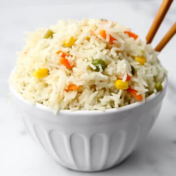 A white bowl filled with Thai coconut rice with carrots, corn, and peas.