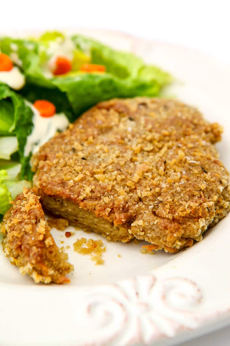A breaded and baked seitan patty on a white plate with salad on the side.