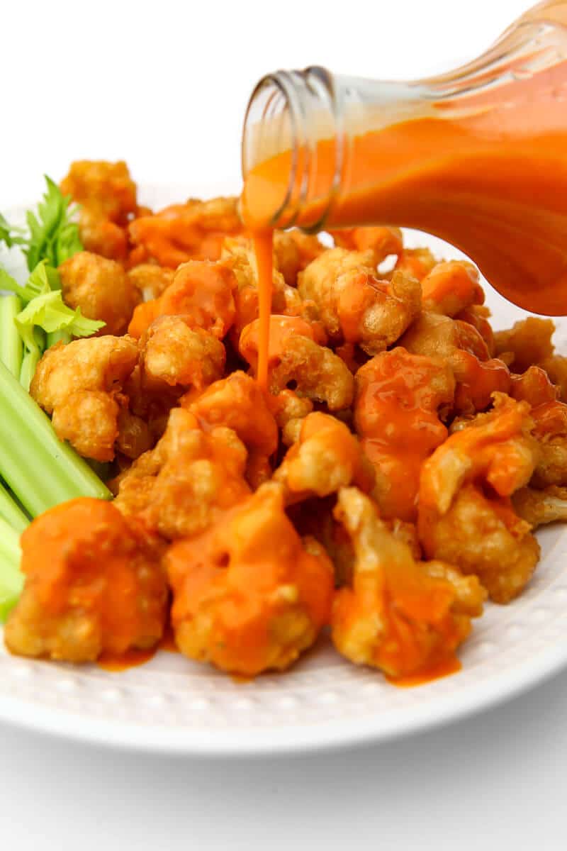 Vegan buffalo sauce being poured over fried cauliflower.