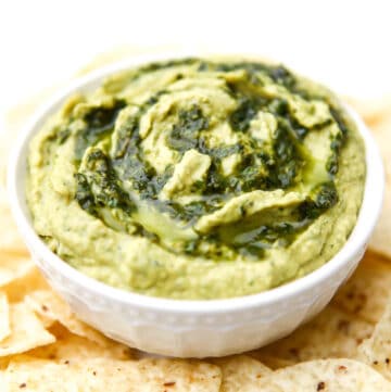 A white bowl filled with pesto hummus with extra pesto swirled on top.