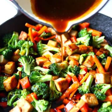 Tofu and stir-fried veggies with homemade teriyaki sauce being poured over it.