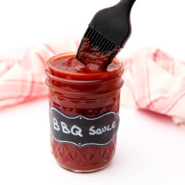 A mason jar filled with homemade BBQ sauce with a kitchen brush dipped in it.