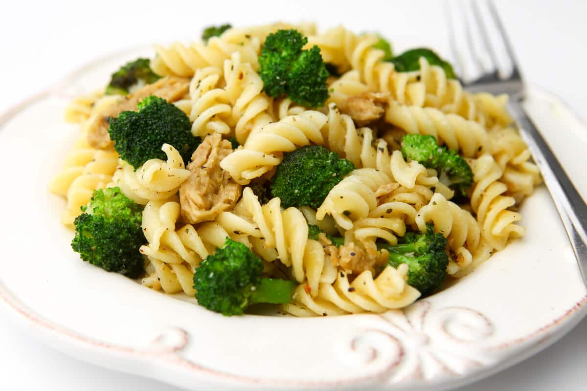 A white plate filled with broccoli pasta with vegan chicken with a fork on the side.