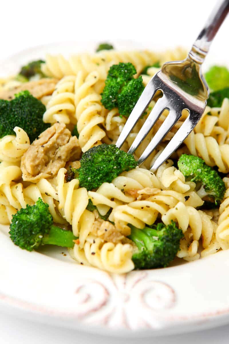 A white plate with broccoli and spiral shaped pasta with a fork sticking in it.