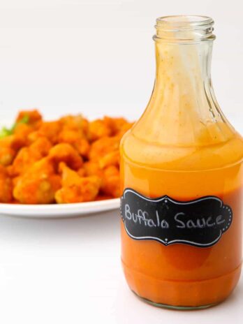 A bottle of vegan buffalo sauce in front of a plate of buffalo cauliflower.
