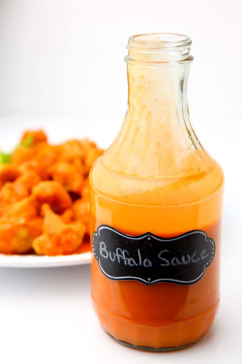 A jar of homemade vegan buffalo sauce in front of vegan buffalo nuggets.