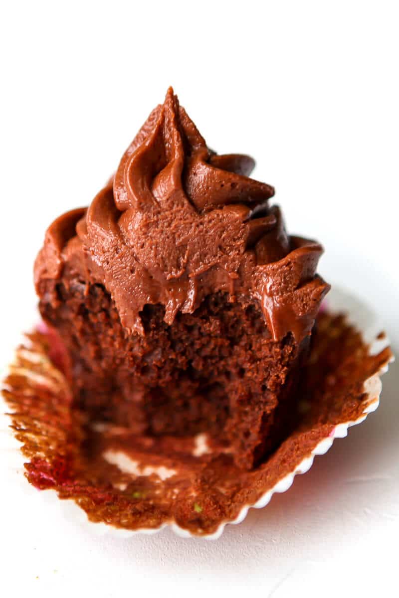 A chocolate cupcake with chocolate frosting with a big bite taken out of it.