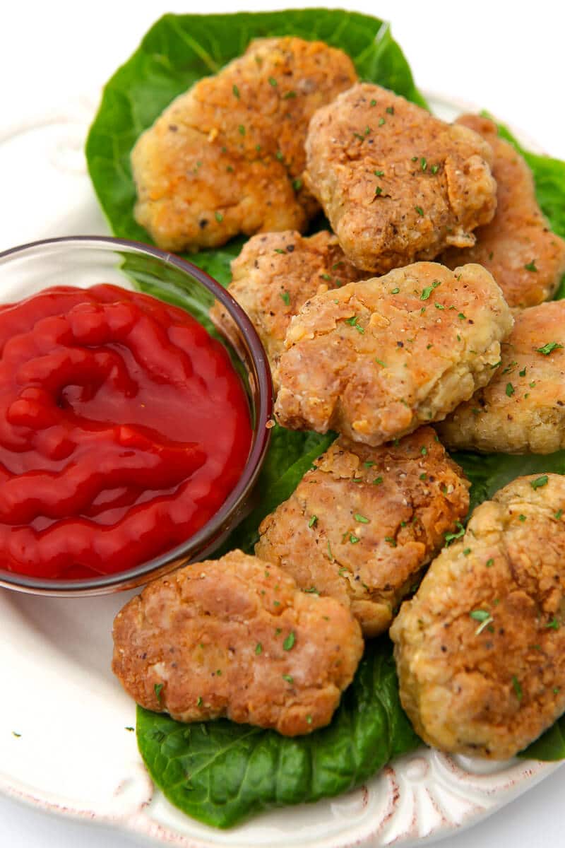 A top view of a white plate filled with vegan chicken nuggets on a bed of lettuce with ketchup on the side.