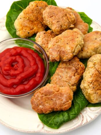 A white plate filled with vegan chicken nuggets on a bed of lettuce with a side of ketchup.