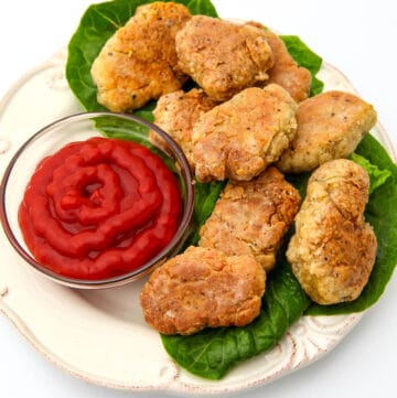 A white plate filled with vegan chicken nuggets on a bed of lettuce with a side of ketchup.