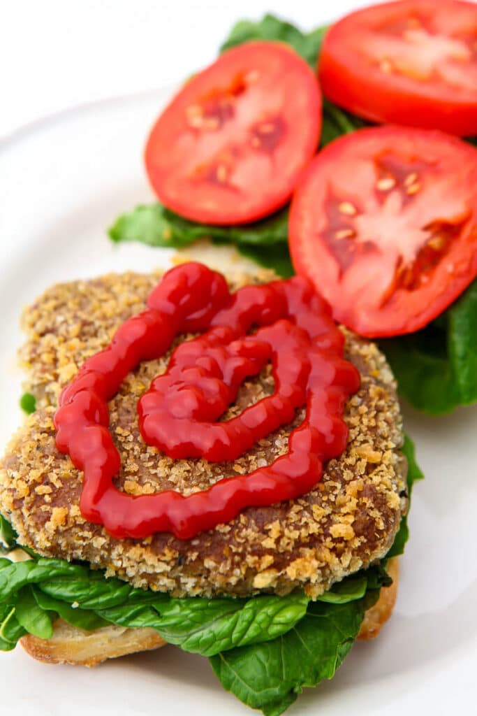 A vegan chicken patty on an open faced bun with lettuce and tomatoes.
