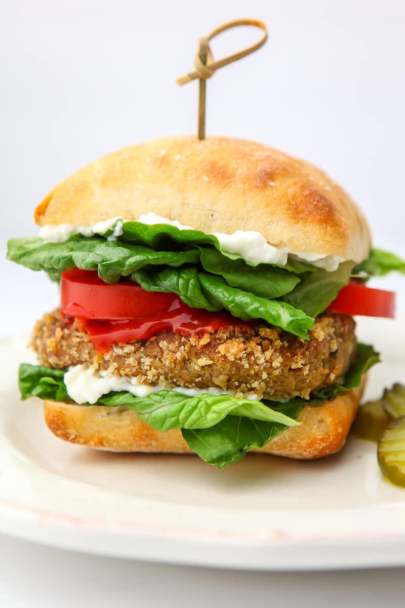 A vegan chicken patty served on a bun with lettuce and tomatoes on a white plate.