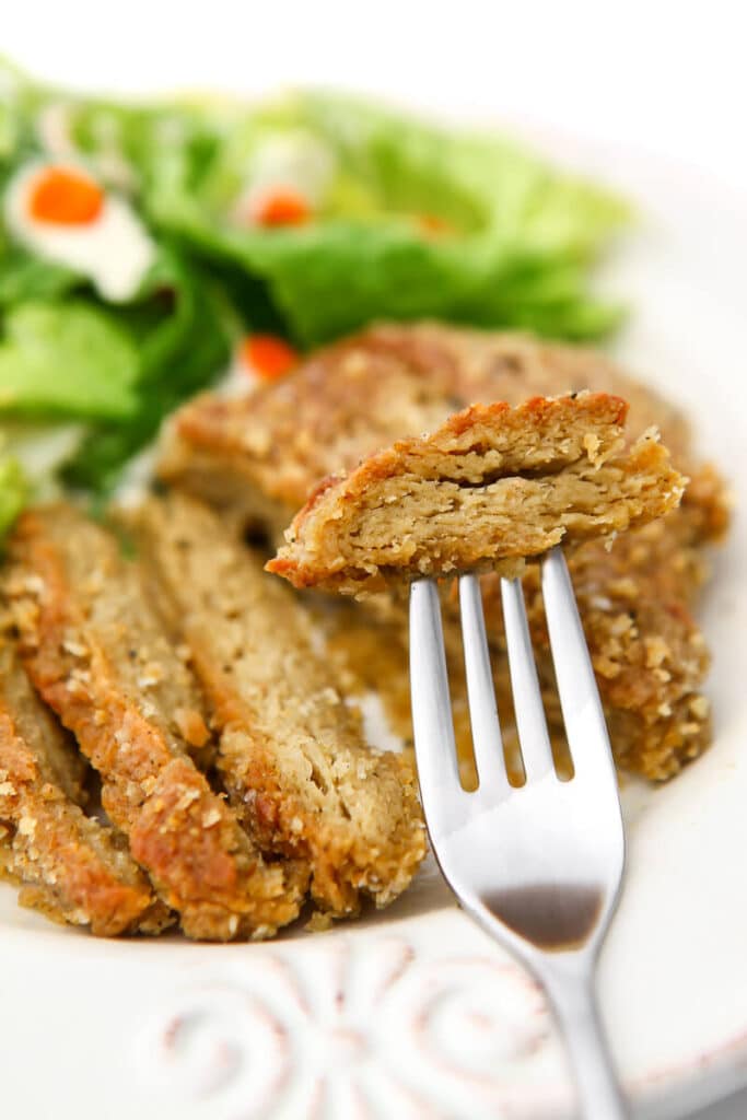 A breaded baked vegan chicken breast cut into slices with a piece on a fork.