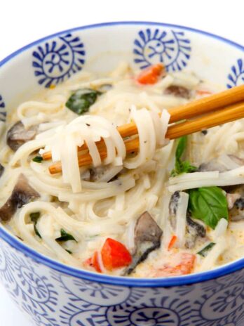 A bowl of coconut curry soup with rice noodles wrapped around chop sticks in a coconut broth.