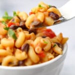 A bowl of spicy vegan mac and cheese with beans and salsa in it.