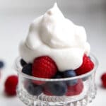 A glass bowl of berries topped with vegan whipped cream made with aquafaba.