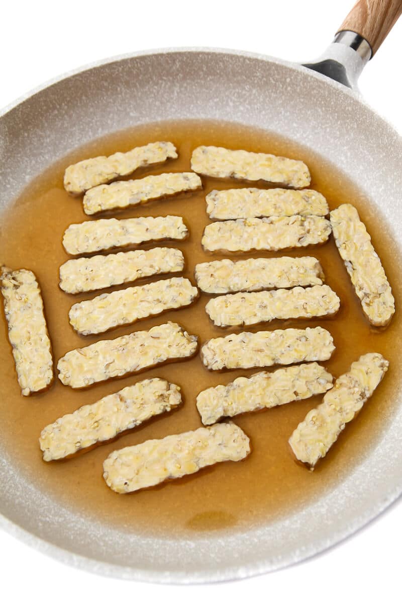 A frying pan with tempeh simmering in broth.