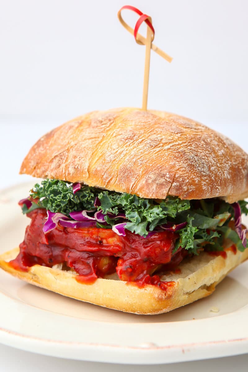 A BBQ tempeh sandwich with shredded kale and purple cabbage on a large roll.